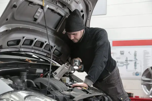 Mechanik samochodowy z latarką bada silnik. Zastanawiasz się, ile zarabia elektronik samochodowy?