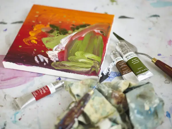 Płótno z barwnym obrazem, tubki farb olejnych Winsor & Newton, paleta i pędzle – idealne narzędzia, by dowiedzieć się, jakimi farbami malować na płótnie.