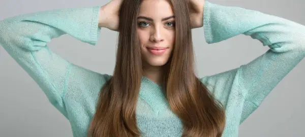 Joven sonríe con las manos en la cabeza, su cabello castaño cae sobre sus hombros. Apenas se notan las primeras canas, un toque de madurez.