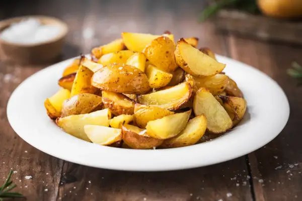 Patate al forno con buccia, dorate e croccanti, servite su un piatto bianco. Un contorno semplice e gustoso.