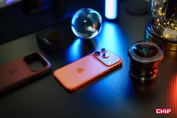 Pomarańczowy iPhone, skórzane etui i obiektyw na czarnym blacie. Idealna konfiguracja iPhone dla fotografa.