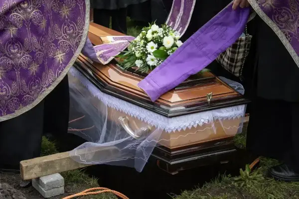 Uroczyste chowanie zmarłego po niedzieli. Trumna z kwiatami, otoczona przez żałobników w strojach liturgicznych, opuszczana do grobu.