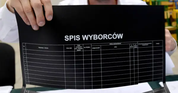 Ręce trzymają czarny dokument z napisem "SPIS WYBORCÓW". Widoczne kolumny do uzupełnienia, sugerujące dopisanie do spisu wyborców.