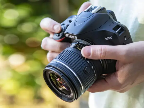 Mani che impugnano una Nikon D3500 con obiettivo 18-55mm. Dettagli sulla nikon d3500 scheda tecnica.