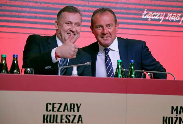 Cezary Kulesza, z synem, uśmiechnięci, z kciukiem w górze, podczas konferencji.