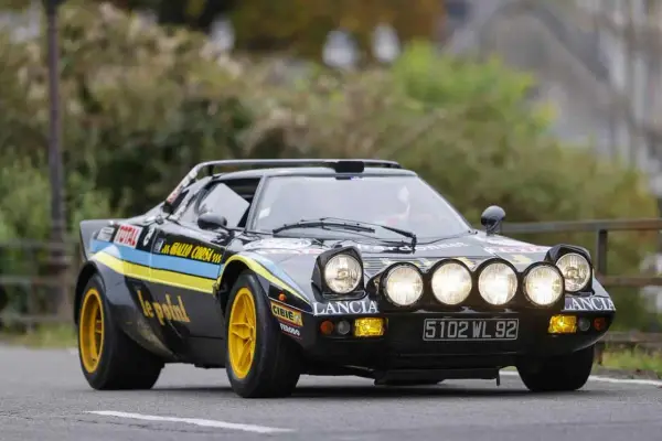 Czarny Lancia Stratos z żółtymi felgami i rajdowymi oznaczeniami, gotowy do pokonania kolejnego zakrętu.
