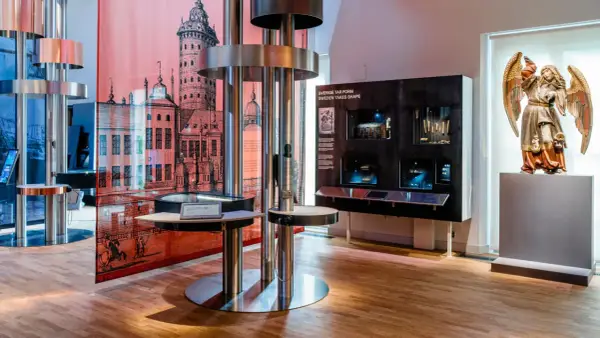 Utställning på ekonomiska museet med en stor illustration av en stad, en skulptur av en ängel och interaktiva displayer.