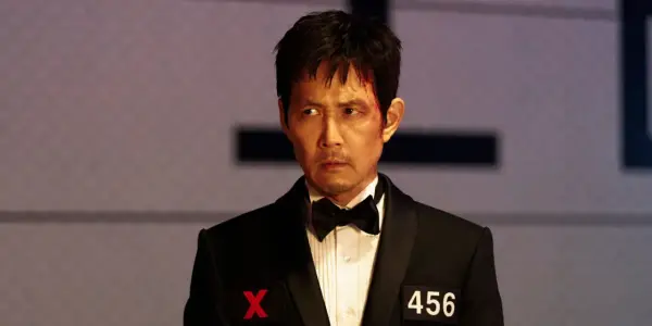 Zraniony Seong Gi-hun w garniturze z numerem 456 i symbolem X, gotowy na kolejne wyzwania w Squid Game sezon 4.