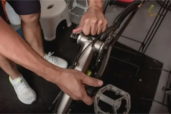 Ręce majsterkowicza przy rowerze, pokazujące, jak zdjąć korbę. Widoczne narzędzia i elementy mechanizmu korbowego.