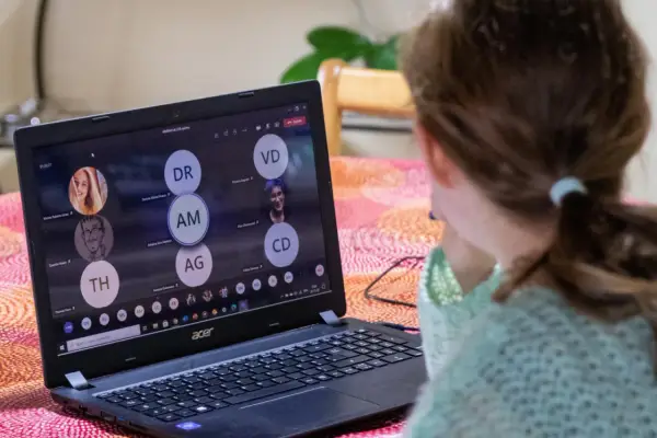 Dziewczynka uczestniczy w lekcji online przez msteams. Na ekranie laptopa widać wiele okręgów z inicjałami uczestników.