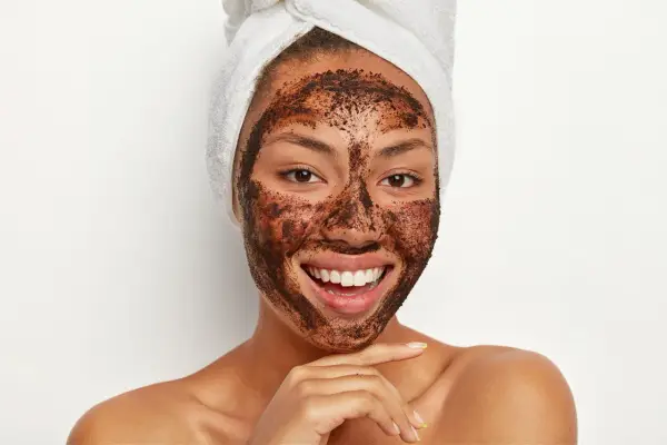 Uśmiechnięta kobieta z ręcznikiem na głowie ma na twarzy naturalny peeling z kawy.