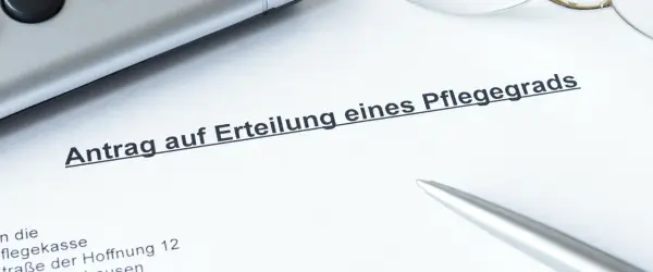 Ein Dokument mit der Überschrift "Antrag auf Erteilung eines Pflegegrads" liegt auf einem Tisch. Daneben liegen ein Stift und eine Brille.