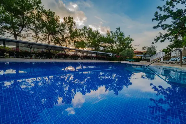 Błękitny basen z odbiciem drzew i chmur. Idealne miejsce na wakacje, zgodnie z **Senza Garden Holiday Club opinie**.