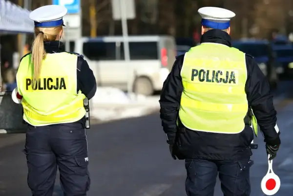 Dwóch policjantów w kamizelkach odblaskowych z napisem "POLICJA" stoi na drodze.