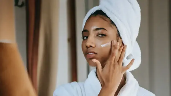 Mujer con toalla en la cabeza aplicándose crema para combatir la piel seca.