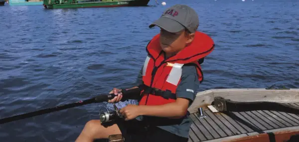 Un enfant pêche en mer, portant un gilet de sauvetage obligatoire. La question du gilet de sauvetage obligatoire jusqu'à quel âge est cruciale pour la sécurité nautique.