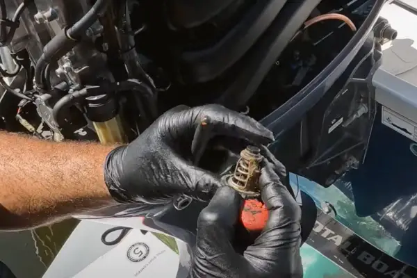 Mains gantées tenant un thermostat usagé, prêt pour le changement sur un moteur hors bord Yamaha.
