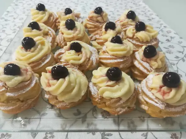 Zeppole pugliesi, dolci fritti con crema pasticcera e ciliegina, spolverati di zucchero a velo.