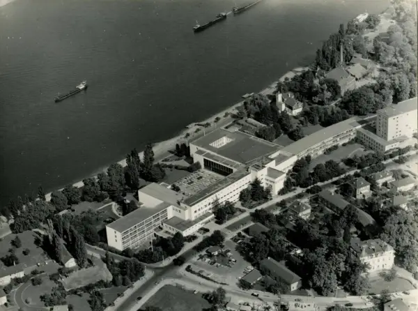 Luftaufnahme von Bonn am Rhein, als die Stadt Hauptstadt war. Mehrere Schiffe auf dem Wasser, Regierungsgebäude und Bäume.