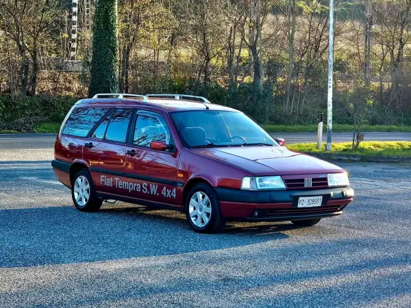 Ciemnoczerwony Fiat Tempra S.W. 4x4 z relingami dachowymi zaparkowany na tle drzew.