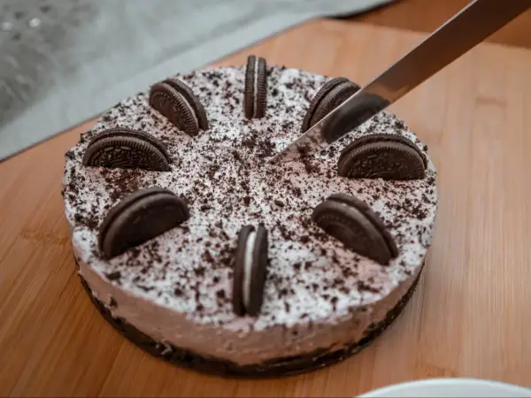 Pyszny sernik oreo, ozdobiony ciasteczkami i posypką, czeka na pokrojenie.
