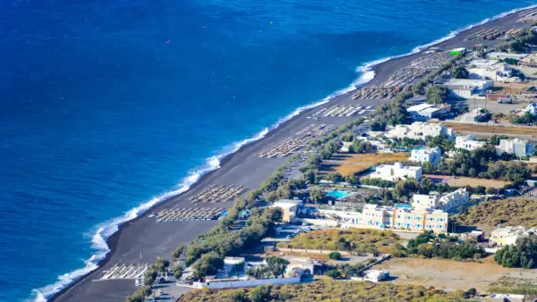 Santorini plaże z czarnym piaskiem, rzędy leżaków i białe budynki hotelowe nad turkusowym morzem.