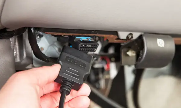 Ręka podłącza kabel OBD II do złącza diagnostycznego pojazdu, aby sprawdzić błędy DTC.