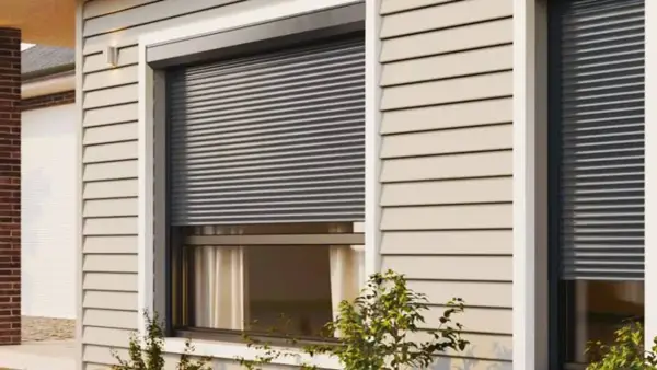 Volet roulant gris fermé sur une fenêtre de maison avec bardage beige.