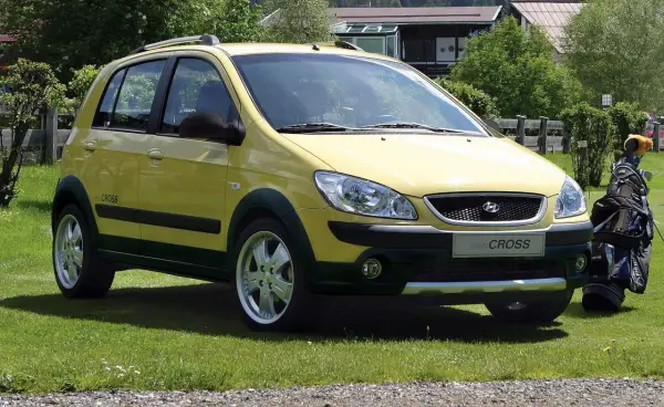 Żółty Hyundai Getz Cross zaparkowany na trawie obok torby golfowej.