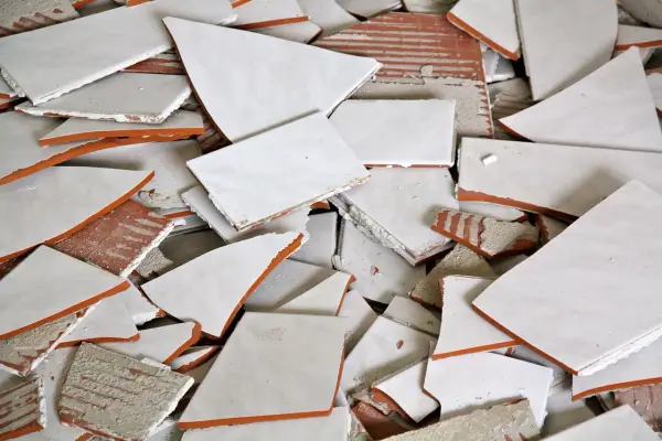 Stos białych, połamanych płytek ceramicznych z pomarańczowymi krawędziami. Wskazówka, jak zdjąć płytki ze ściany bez uszkodzenia.