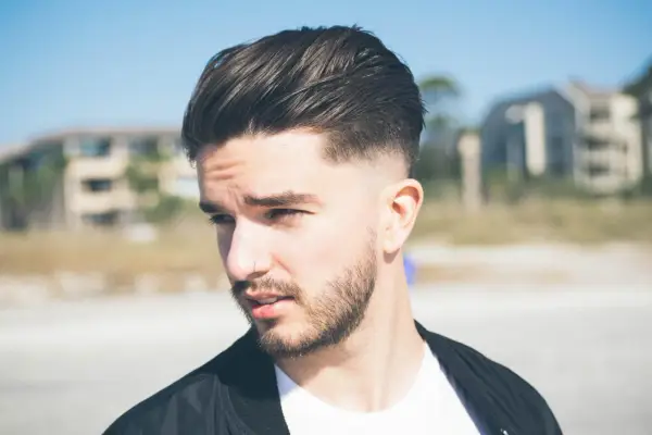 Joven con barba y cortes de pelo hombre elegante, peinado hacia atrás con degradado.
