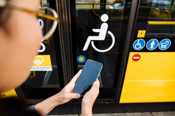 Osoba trzyma telefon przed drzwiami autobusu z symbolem wózka inwalidzkiego. To ułatwia podróżowanie, gdy masz legitymację osoby niepełnosprawnej.