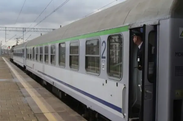 Konduktor w czapce stoi w otwartych drzwiach pociągu z zieloną górą, gotowy do odjazdu ze Szczecina.