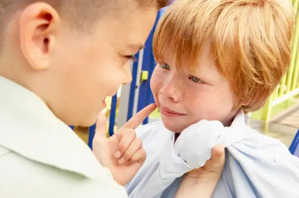 Ein Junge zeigt mit dem Finger auf das Gesicht eines anderen Jungen, der verängstigt wirkt. Ein Beispiel für Mobbing in der Schule.