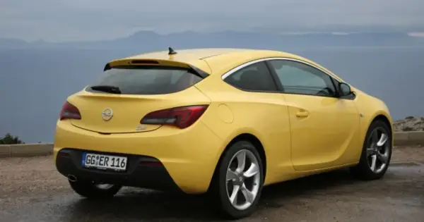 Żółta Astra GTC z tablicą rejestracyjną GG ER 116 stoi na tle morza i gór.