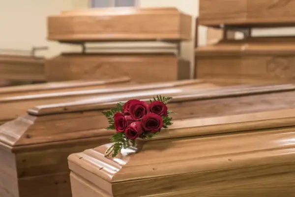 Wiele rodzajów trumien, niektóre ułożone piętrowo. Na jednej z nich bukiet czerwonych róż i złota obręcz.