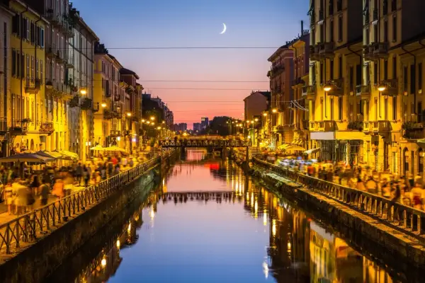 Atardecer en los Navigli de Milán, con gente paseando y luces reflejándose en el canal.
