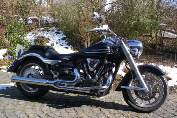 Błyszczący czarny motocykl Yamaha Raider 1900, z chromowanymi detalami, zaparkowany na bruku. W tle zima i krzewy.