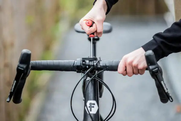 Hände stellen den MTB Lenker ein. Mit einem Schraubenzieher wird die Lenkerposition justiert, um die perfekte Fahrt zu ermöglichen.