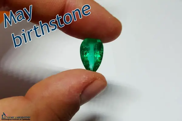 Fingers hold a pear-shaped emerald, the vibrant green gem representing the May birthstone.