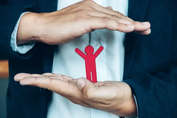 Dłonie obejmujące czerwoną postać symbolizują opiekę i odpowiedzialność za drugiego człowieka.