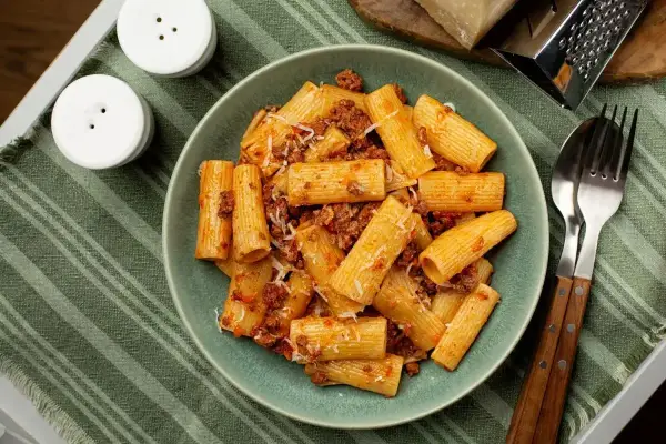 Pyszne makaron grube rurki z sosem bolońskim i parmezanem, gotowe do jedzenia.