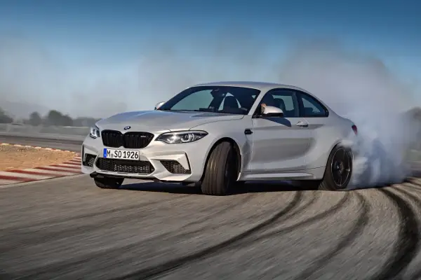 Un BMW M2 Competition CV derrapa en una pista, dejando estelas de humo y marcas de neumáticos.