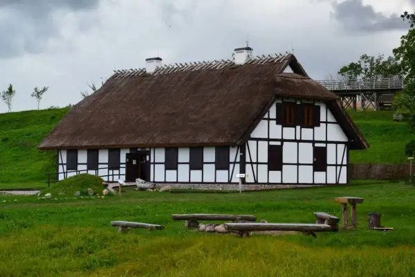 Rzucewo osada łowców fok. Dom z muru pruskiego i strzechą, otoczony zielenią, z ławkami i stołem w trawie.