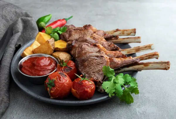 A perfectly grilled comber jagnięcy, served with roasted tomatoes, potato wedges, chili peppers, and a side of ketchup.