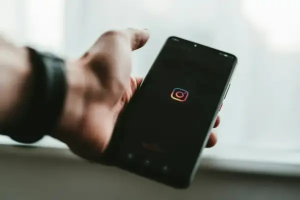 Dłoń trzyma smartfon z logo Instagram. Chcesz wiedzieć, jak zobaczyć relacje na IG?