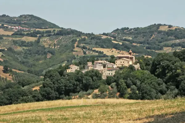 Borgo collinare di **Cerreto di Saludecio** con case in pietra e una chiesa, immerso nel verde della campagna romagnola.