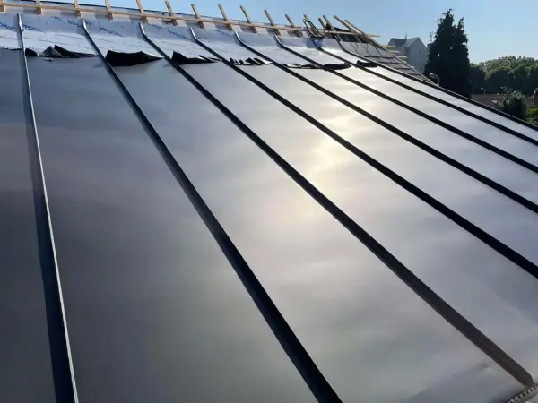 Pose de feuilles de toit en zinc sur une nouvelle construction. Le soleil brille sur le métal lisse.