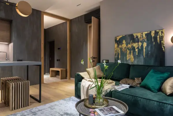 Elegancki salon z butelkowozieloną kanapą, na której leży kot. Złoto-granatowy obraz i jasne dodatki pokazują, jaki kolor pasuje do zielonego butelkowego.