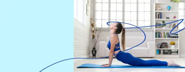 Kobieta w niebieskim stroju wykonuje rozciąganie statyczne na macie. Pozycja kobra pogłębia wygięcie kręgosłupa.